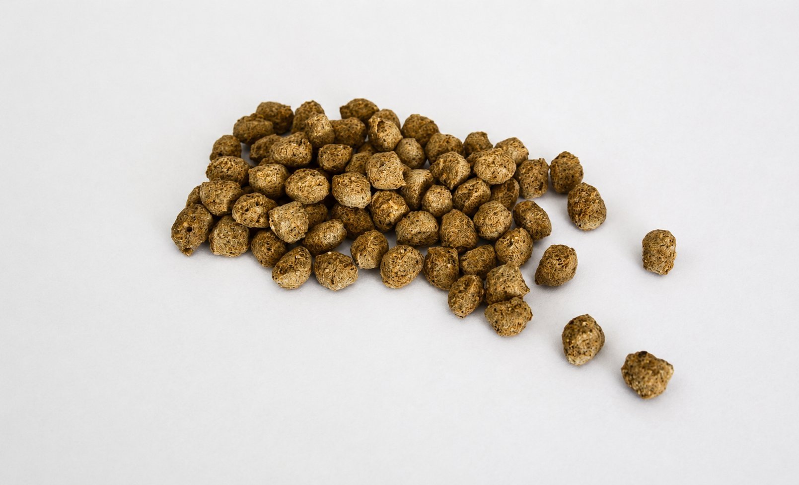 Pile of brown pet kibble or cereal balls on white background with some scattered pieces